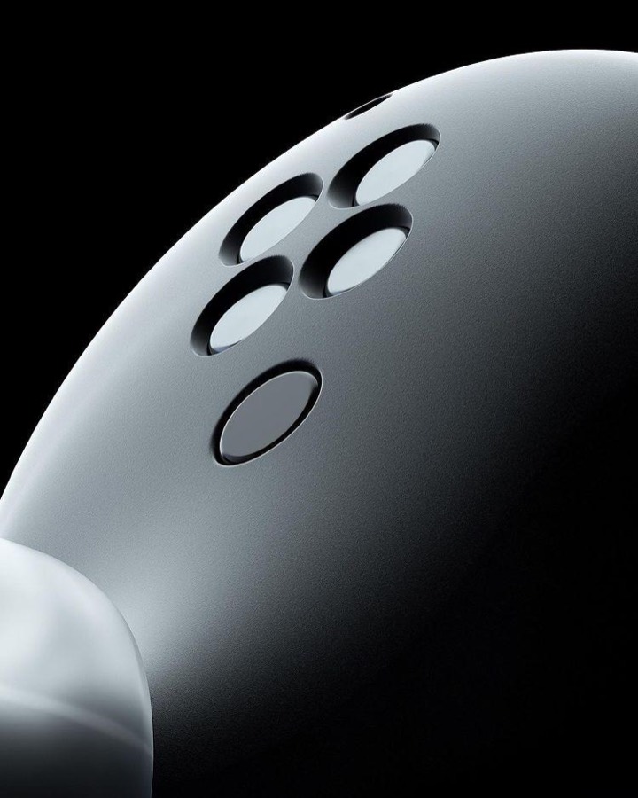 Extreme close-up of a matte black rounded device, speaker holes and lens catching a single soft highlight against pure black.